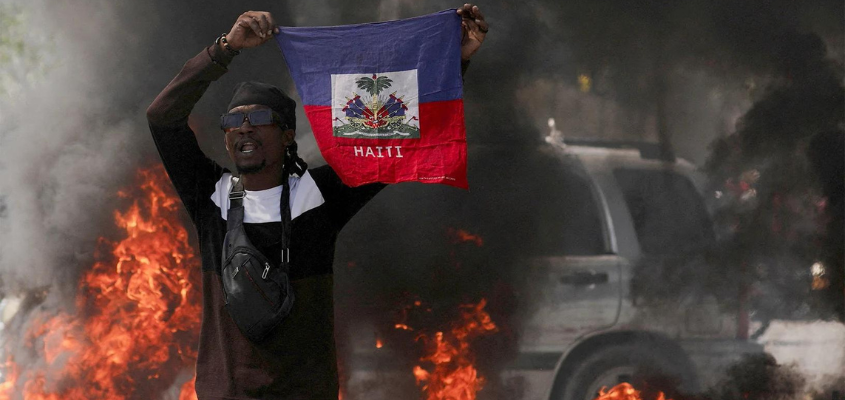 Man holding Haitian flag in front of a fire