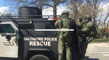 A police tactical vehicle leaves the scene with officers in fatigues hanging on